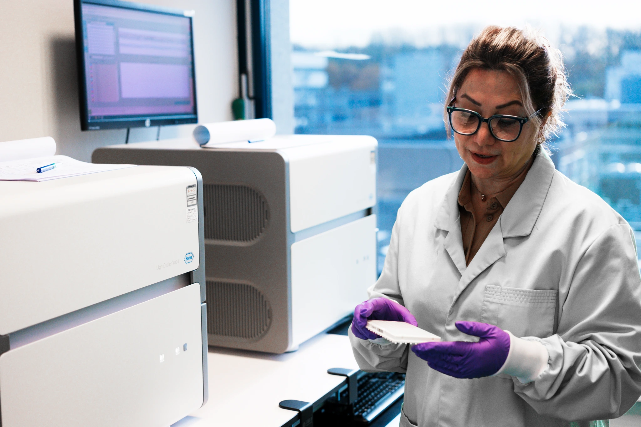 Medium shot of female scientist holding microplate beside analyser
