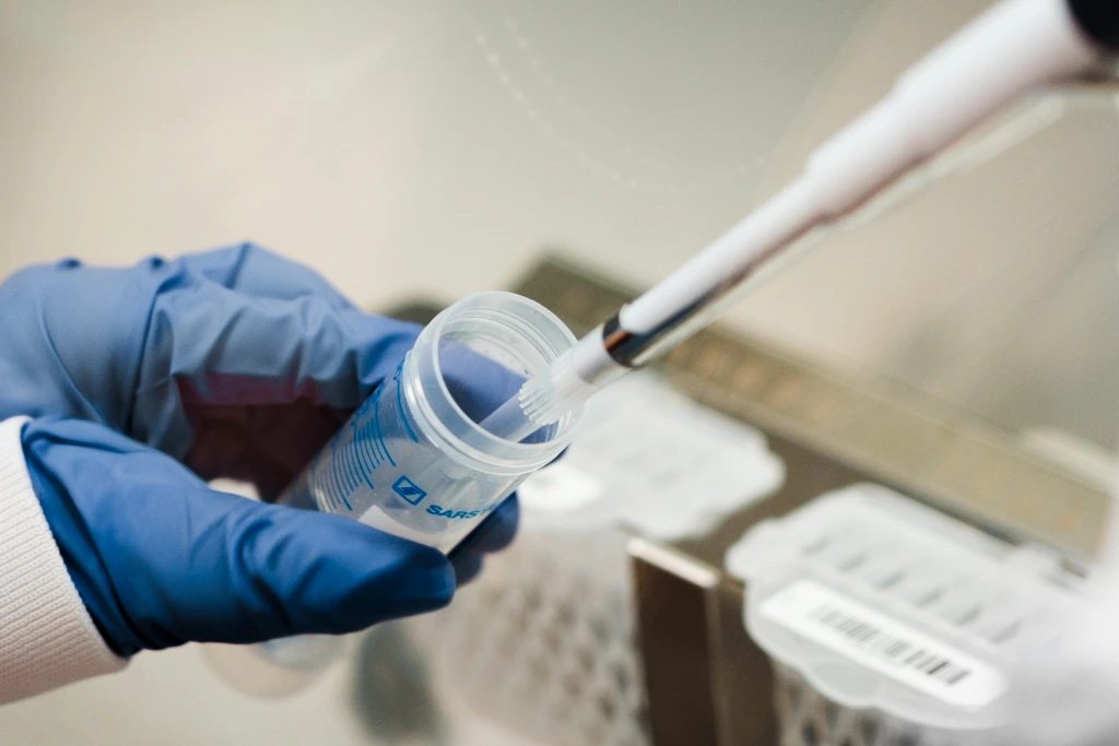 Close up of gloved hand pipetting into sample container
