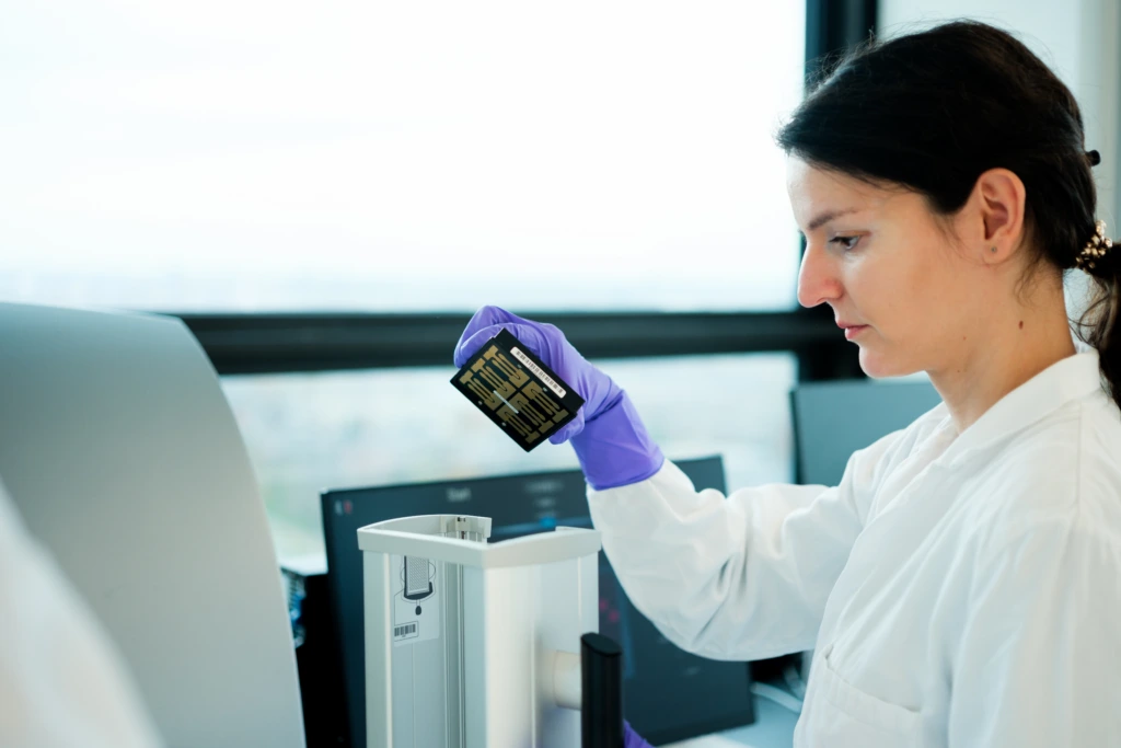 Scientist holding laboratory microplate tray beside analyser