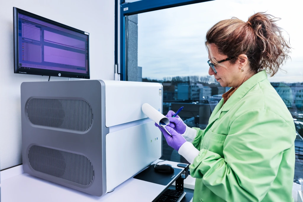 Medium shot of female scientist in green lab coat at laboratory analyser