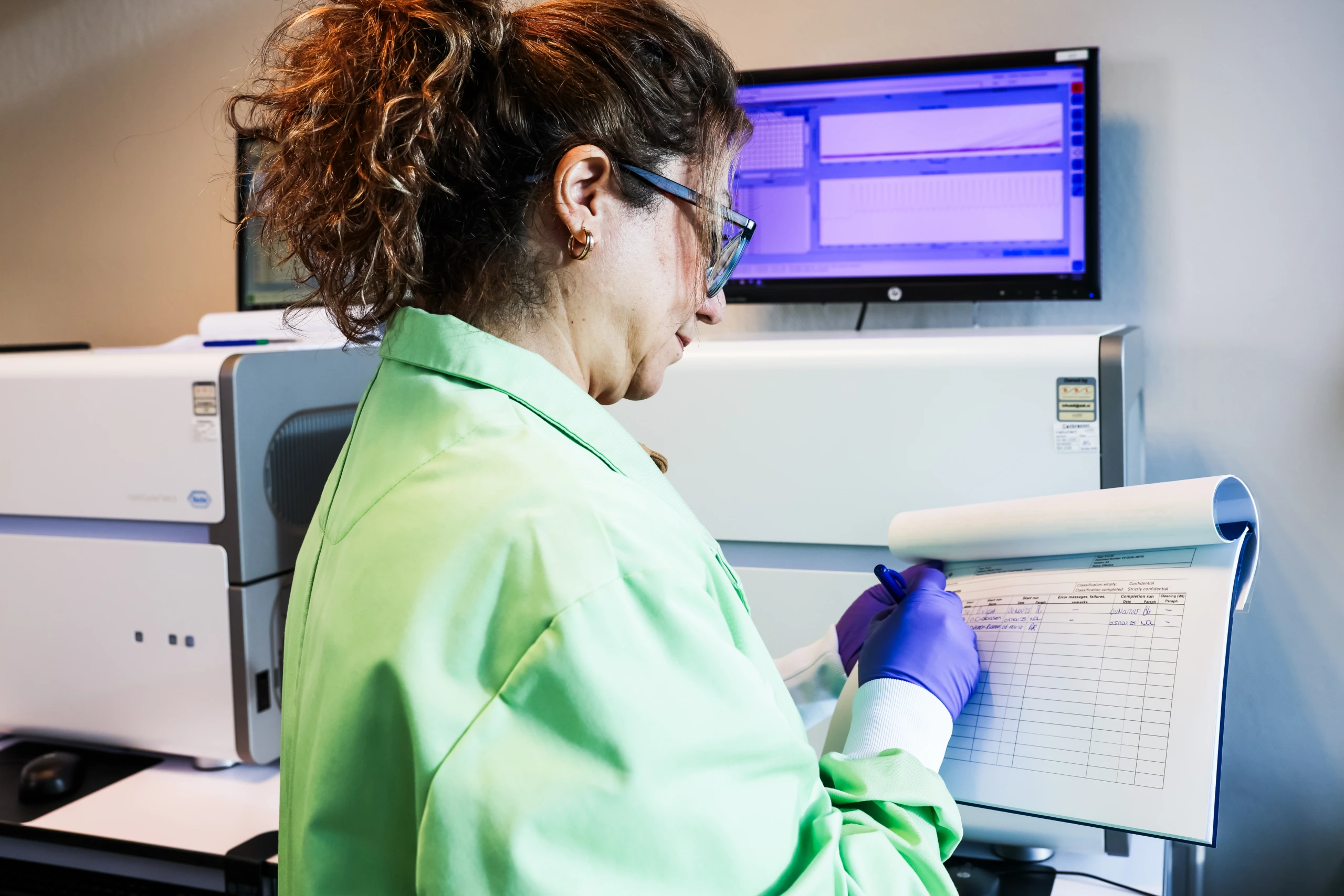 Medium close up of female scientist in green coat at laboratory analyser