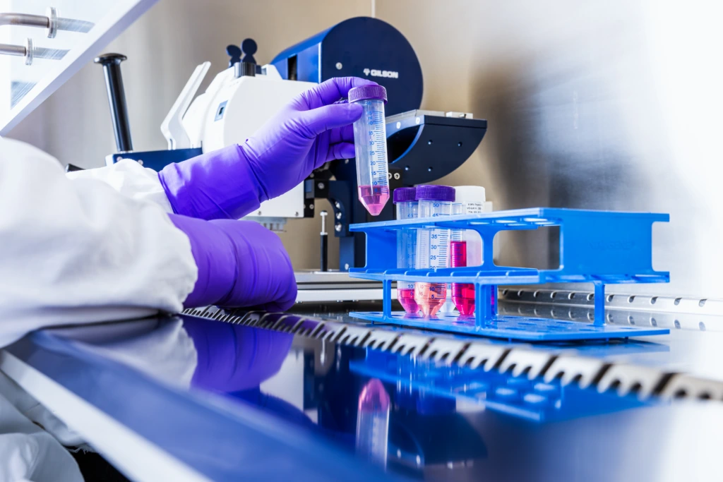 Close up of purple-gloved hands loading red-filled plate into laboratory automation system