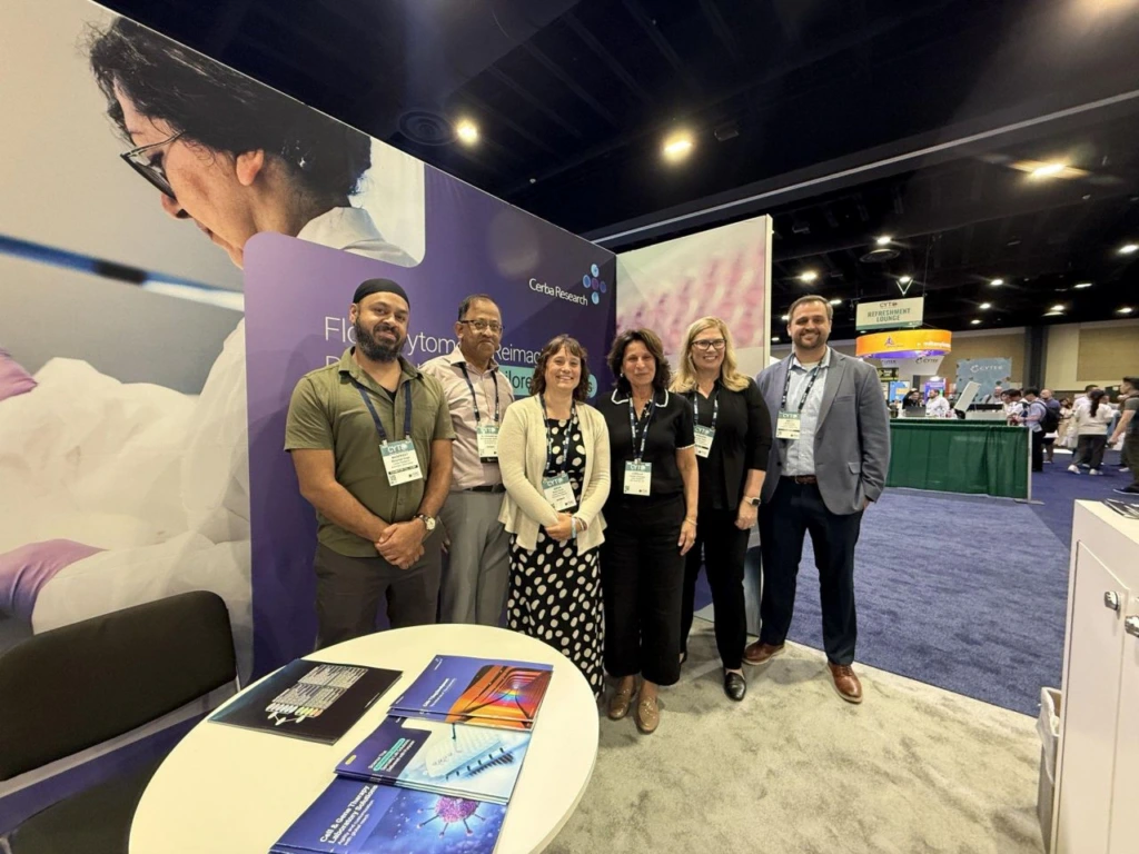 A group of six Cerba Research employees stand in front of an exhibition booth inside a conference building, smiling at the camera.